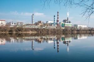 tubi della segheria dell'impianto di impresa di lavorazione del legno vicino al fiume. concetto di inquinamento atmosferico. paesaggio industriale inquinamento ambientale rifiuti di centrale termica foto