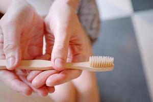 primo piano delle mani della donna che tengono uno spazzolino da denti in legno di bambù, uno stile di vita sostenibile, un concetto di zero rifiuti foto