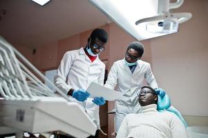 paziente uomo afroamericano in poltrona odontoiatrica. studio dentistico e concetto di pratica medica. dentista professionista che aiuta il suo paziente in odontoiatria medica. indicando la radiografia dei denti. foto