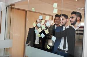 uomo d'affari che punta sul vetro con note di carta colorate. gruppo eterogeneo di dipendenti maschi in abiti formali che utilizzano adesivi. foto