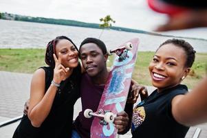 gruppo di tre amici afroamericani con skateboard che fanno selfie sul telefono. foto