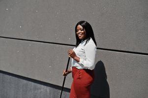 donna d'affari afroamericana formalmente vestita in camicetta bianca e pantaloni rossi con bastone da passeggio a portata di mano. imprenditrice di successo dalla pelle scura. foto