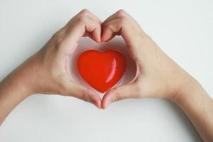 una donna fa la sua mano a forma di cuore che copre un cuore rosso con uno sfondo bianco. idea di donazione foto