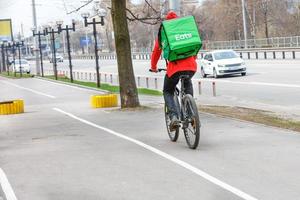 corriere con uno zaino verde isotermico sulla schiena su una bicicletta per la consegna di cibo in una strada cittadina. foto