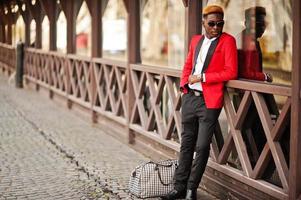 moda uomo afroamericano modello in abito rosso, con capelli in evidenza e borsa in posa in strada. foto