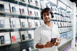 l'acquirente del cliente uomo indiano presso il negozio di telefoni cellulari ascolta la musica dagli auricolari wireless collegati al suo smartphone. concetto di popoli e tecnologie dell'Asia meridionale. negozio di cellulari. foto