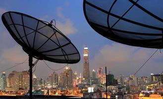 antenna parabolica nera di comunicazione sopra il cielo al tramonto nel paesaggio urbano foto