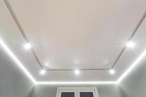 controsoffitto con lampade alogene e costruzione di cartongesso in una stanza vuota in appartamento o casa. soffitto teso bianco e di forma complessa. foto