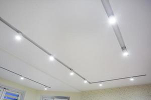 lampade alogene su controsoffitto e costruzione di muri a secco in stanze vuote in appartamenti o case. soffitto teso bianco e di forma complessa. foto