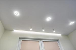 lampade alogene su controsoffitto e costruzione di muri a secco in stanze vuote in appartamenti o case. soffitto teso bianco e di forma complessa. foto