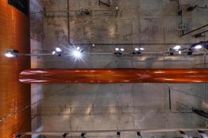 alzando lo sguardo sul soffitto in cemento grigio con faretti alogeni e lampade edison in un ufficio loft con aria condizionata e tubo di ventilazione arancione foto