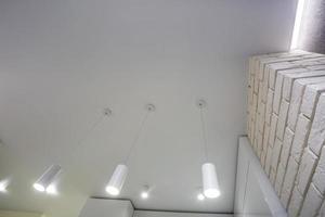 lampade alogene su controsoffitto e costruzione di muri a secco in stanze vuote in appartamenti o case. soffitto teso bianco e di forma complessa. foto