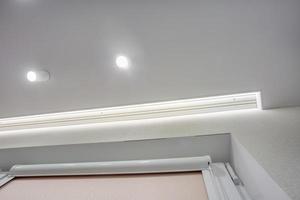 lampade alogene su controsoffitto e costruzione di muri a secco in stanze vuote in appartamenti o case. soffitto teso bianco e di forma complessa. foto