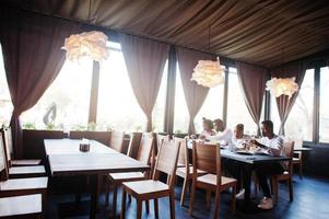 felici amici africani seduti, chiacchierando al bar e mangiando cibo. gruppo di persone di colore che si incontrano al ristorante e cenano. foto