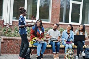 gruppo di cinque studenti universitari africani che trascorrono del tempo insieme nel campus nel cortile dell'università. amici afro neri che studiano al banco con articoli per la scuola, notebook portatili. foto