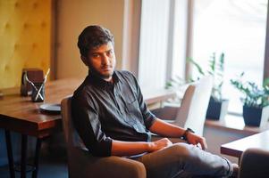 fiducioso giovane indiano in camicia nera seduto al caffè. foto