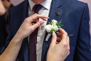 la sposa mette lo sposo su un fiore all'occhiello di rosa e rosa bianca il giorno del matrimonio foto