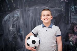 ragazzo felice che tiene un pallone da calcio davanti alla lavagna foto