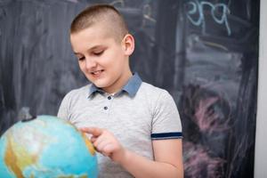 ragazzo che usa il globo terrestre davanti alla lavagna foto