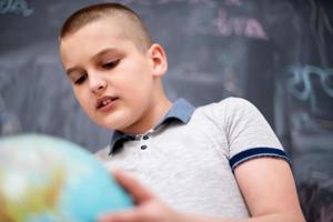 ragazzo che usa il globo terrestre davanti alla lavagna foto