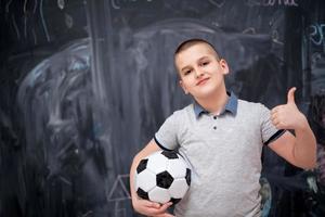 ragazzo felice che tiene un pallone da calcio davanti alla lavagna foto