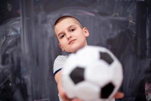 ragazzo felice che tiene un pallone da calcio davanti alla lavagna foto