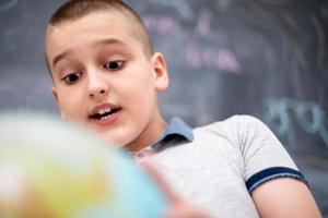 ragazzo che usa il globo terrestre davanti alla lavagna foto