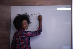 donna afroamericana che scrive su una lavagna in un ufficio moderno foto