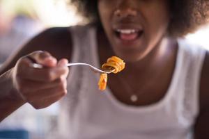 una giovane donna afroamericana che mangia pasta foto