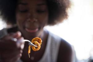 una giovane donna afroamericana che mangia pasta foto