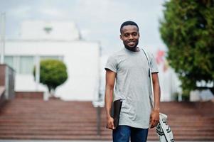 studente africano maschio posato con zaino e articoli per la scuola nel cortile dell'università, contro le bandiere di diversi paesi. foto