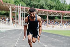 atleta maschio afroamericano in abbigliamento sportivo che corre da solo lungo una pista da corsa allo stadio.