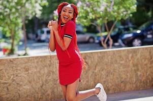 ragazza afroamericana carina e snella in vestito rosso con i dreadlocks in movimento divertendosi per strada. modello nero elegante. foto