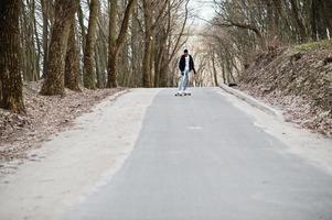 uomo arabo in stile street con occhiali da vista con longboard longboard lungo la strada. foto