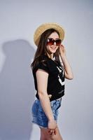 ritratto di una ragazza attraente in maglietta nera che dice lol, pantaloncini di jeans, cappello e occhiali da sole in posa in studio. foto