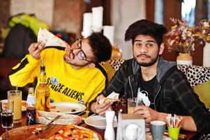 ragazzi asiatici di amici che mangiano pizza durante la festa in pizzeria. felici indiani che si divertono insieme, mangiano cibo italiano e si siedono sul divano. foto