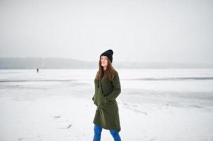ragazza divertente indossare su felpa verde lunga, jeans e copricapo nero, al lago ghiacciato in una giornata invernale. foto