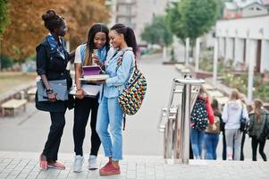 tre studentesse africane hanno posato con zaini e articoli per la scuola nel cortile dell'università e guardano il tablet. foto