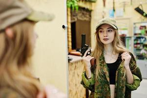 ragazza militare in uniforme mimetica con pistola revolver a portata di mano sullo sfondo dell'esercito sul poligono di tiro. foto