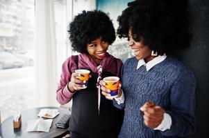 due capelli ricci donna afroamericana indossano maglioni con tazze di tè poste al bar al coperto. foto