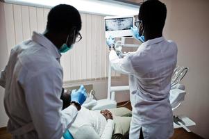 paziente uomo afroamericano in poltrona odontoiatrica. studio dentistico e concetto di pratica medica. dentista professionista che aiuta il suo paziente in odontoiatria medica. indicando la radiografia dei denti. foto