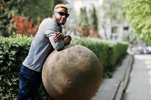 elegante ragazzo afroamericano su maglione grigio e occhiali da sole neri in posa per strada. ragazzo nero alla moda. foto