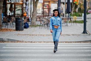 donne afroamericane alla moda alla moda in jeans indossano e berretto nero che camminano sul traffico pedonale. foto