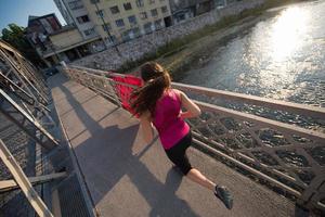 donna che fa jogging attraverso il ponte al mattino soleggiato foto