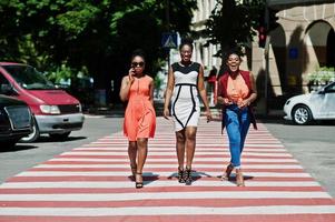 tre eleganti donne afroamericane che camminano sul passaggio pedonale o pedonale, parlando tra loro e divertendosi. foto