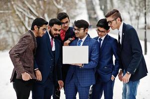 un gruppo di sei uomini d'affari indiani in giacca e cravatta poste all'aperto in una giornata invernale in Europa, guardando sul computer portatile. foto