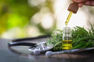 mani del medico che tengono un contagocce con un prodotto petrolifero sullo sfondo delle foglie e fiori di marijuana, olio di canapa cbd. foto