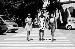 tre eleganti donne afroamericane che camminano sul passaggio pedonale o pedonale, parlando tra loro e divertendosi. foto