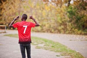 uomo afroamericano in maglietta rossa sportiva da calcio con numero 7 contro il parco autunnale. foto
