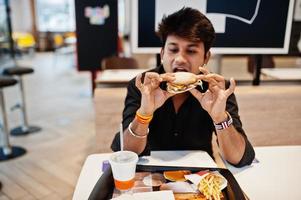 uomo indiano alla moda seduto al fast food cafe e mangiare hamburger. foto